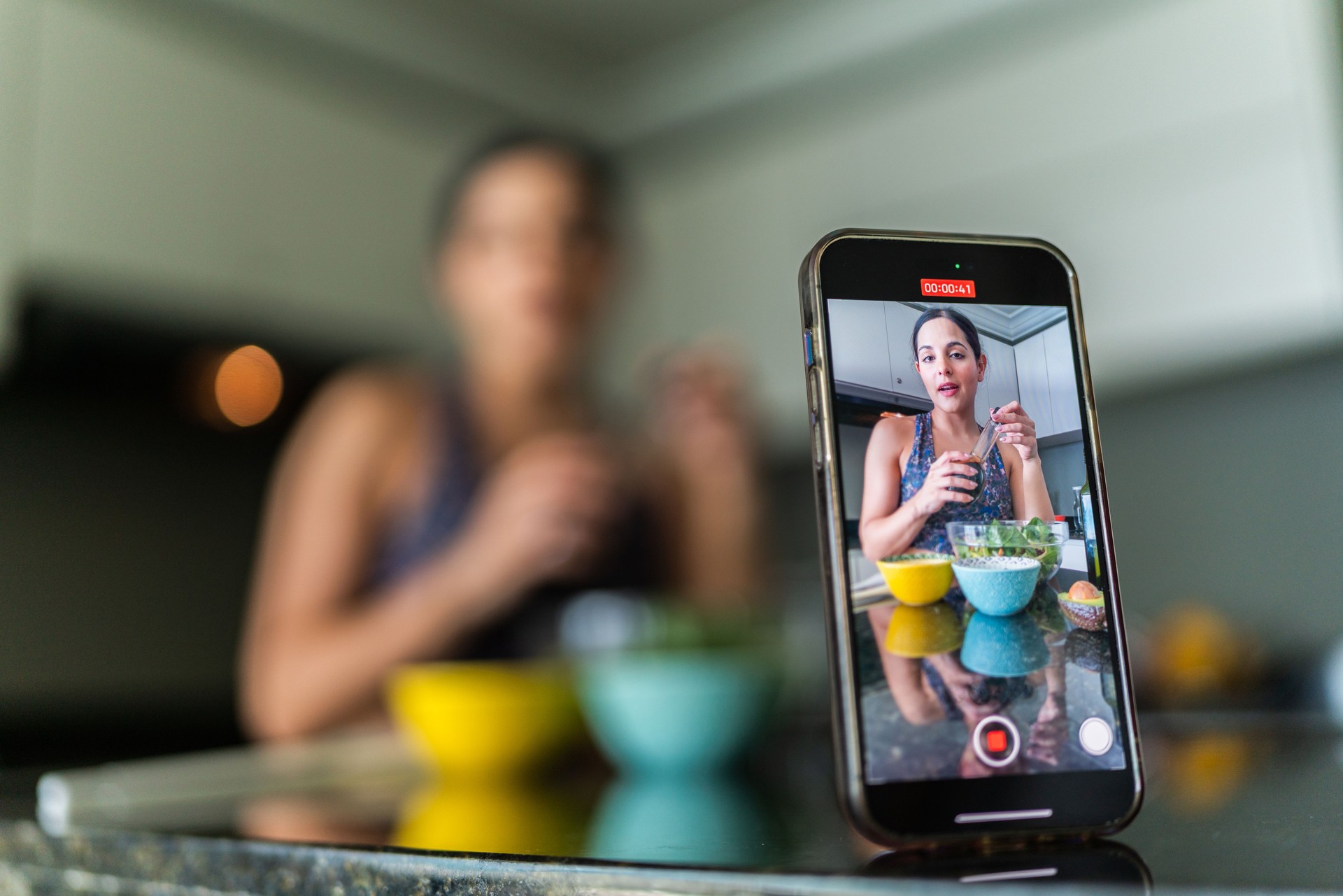 Primer plano de un teléfono móvil grabando un vlog de una mujer joven preparando ensalada en la cocina de su casa